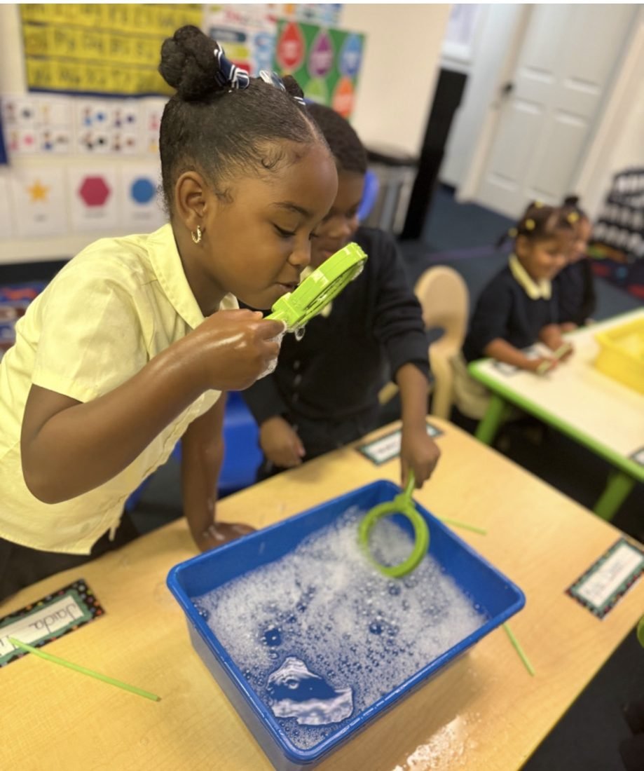 School-age scholar examining bubbles with a magnifying glass during enrichment