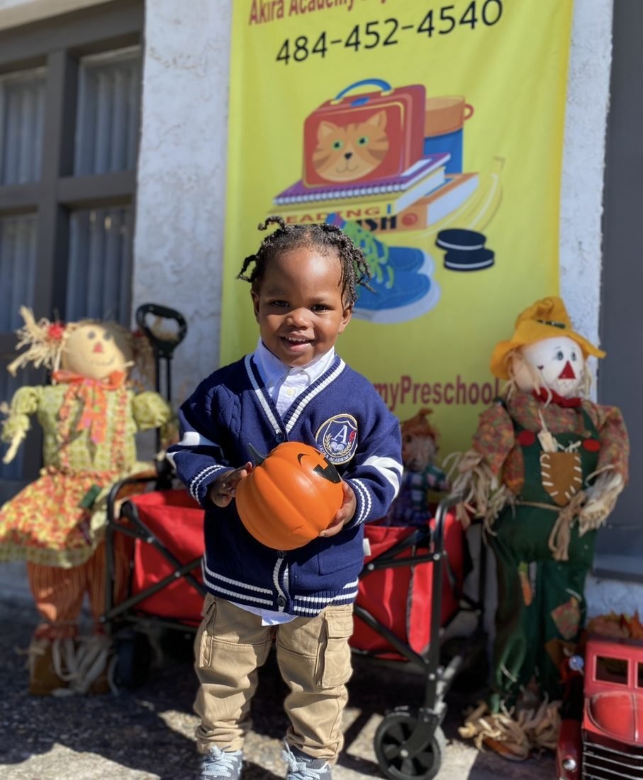 A scholar holding a pumpkin outside Akira Academy during a seasonal event